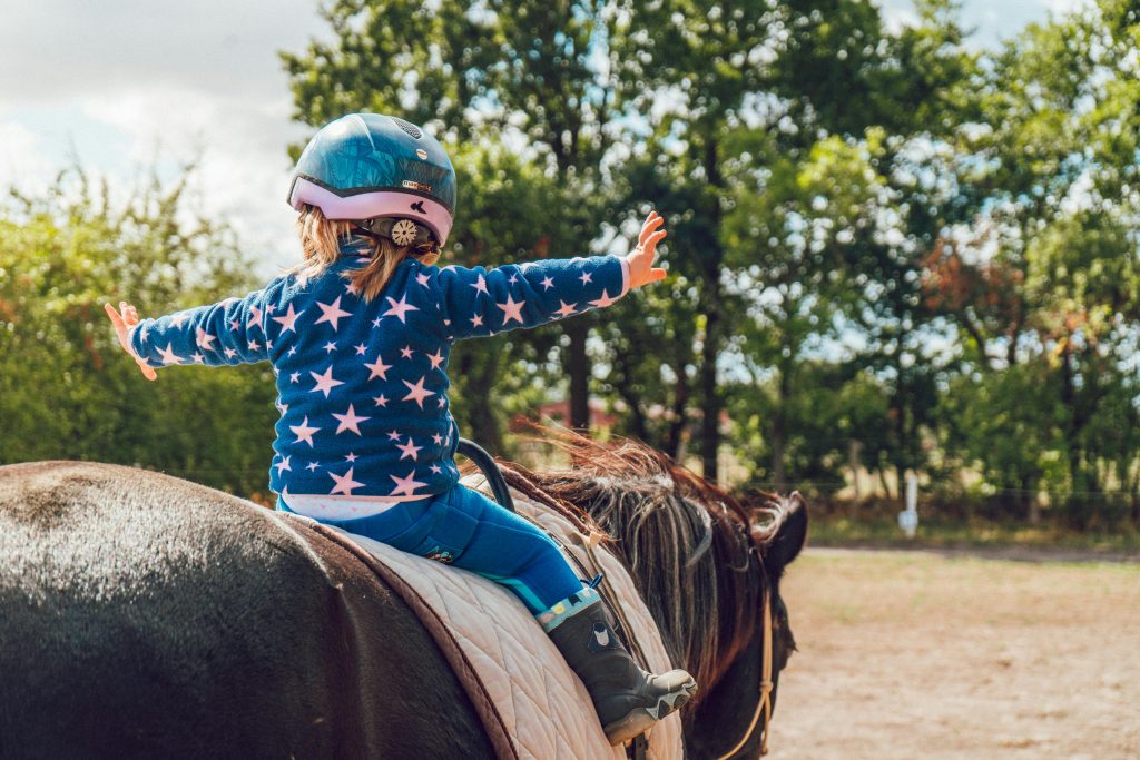 pexels-photo-1364073-1364073 A child confidently rides a horse outdoors, wearing a helmet and star-patterned jacket.